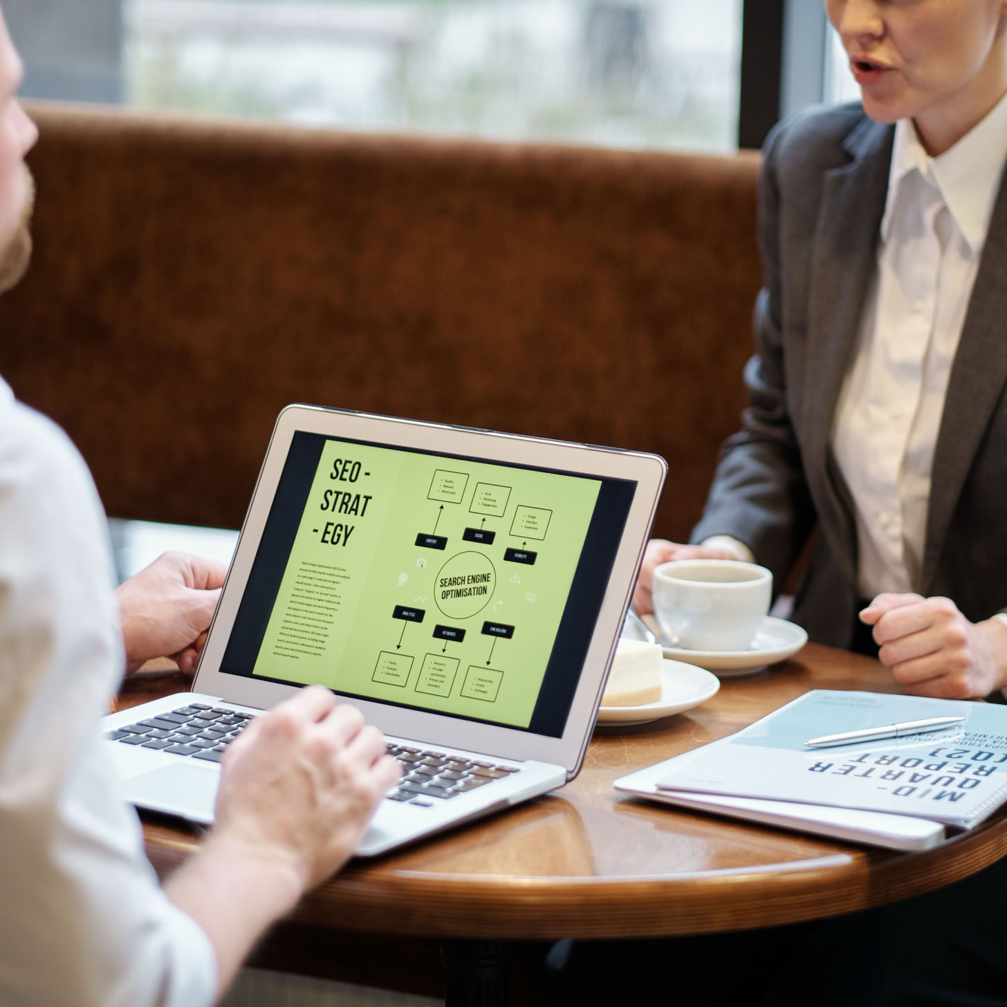 A man and woman engaged in a business meeting discussing SEO strategy in a cozy cafe setting.